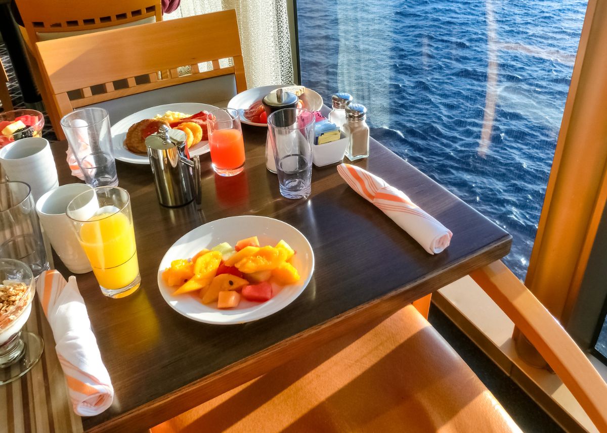 A table next to the window of a cruise ship with food and drinks on it.