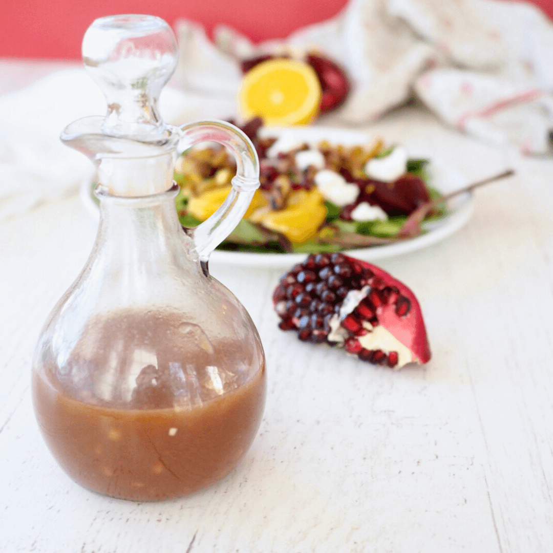 Pomegranate dressing in a glass picture in front of a pomegranate fruit segment.