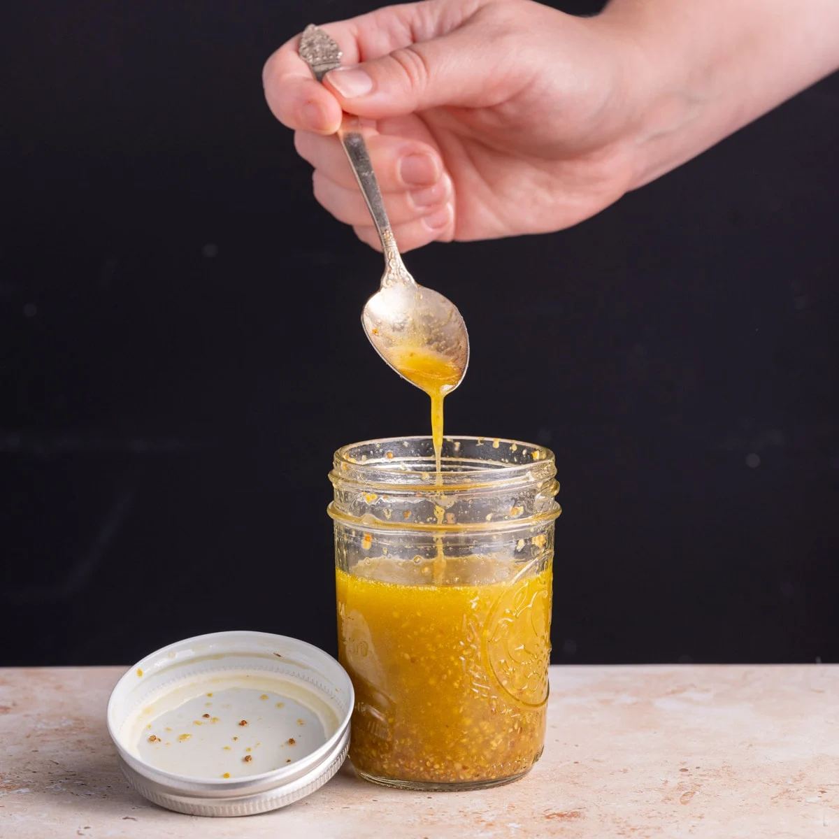 Yellow homemade dressing dropping from a spoon into a mason jar.