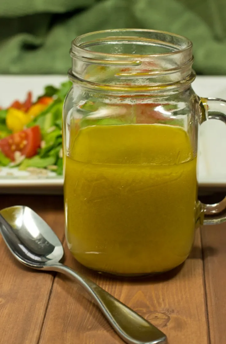 Homemade vinaigrette dressing in a large mason glass jar in from of a plate of salad.
