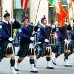 Men in kilts marching in a St. Patrick's Day parade with flags.