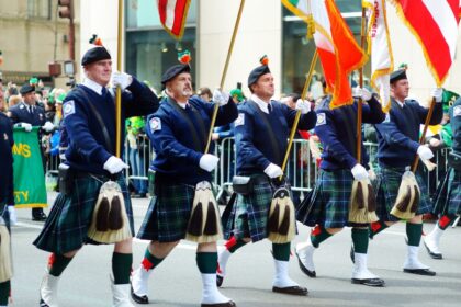 Men in kilts marching in a St. Patrick's Day parade with flags.