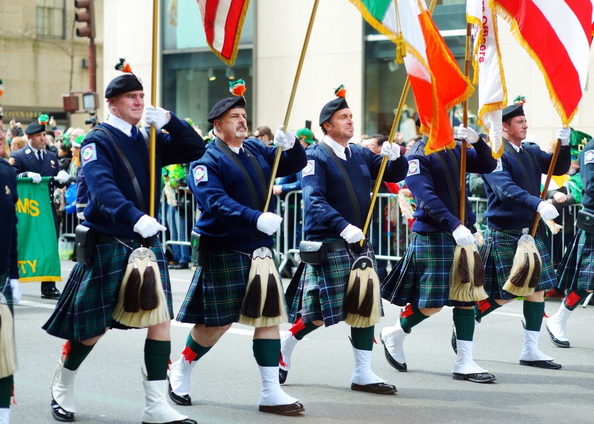 Men in kilts marching in a St. Patrick's Day parade with flags.