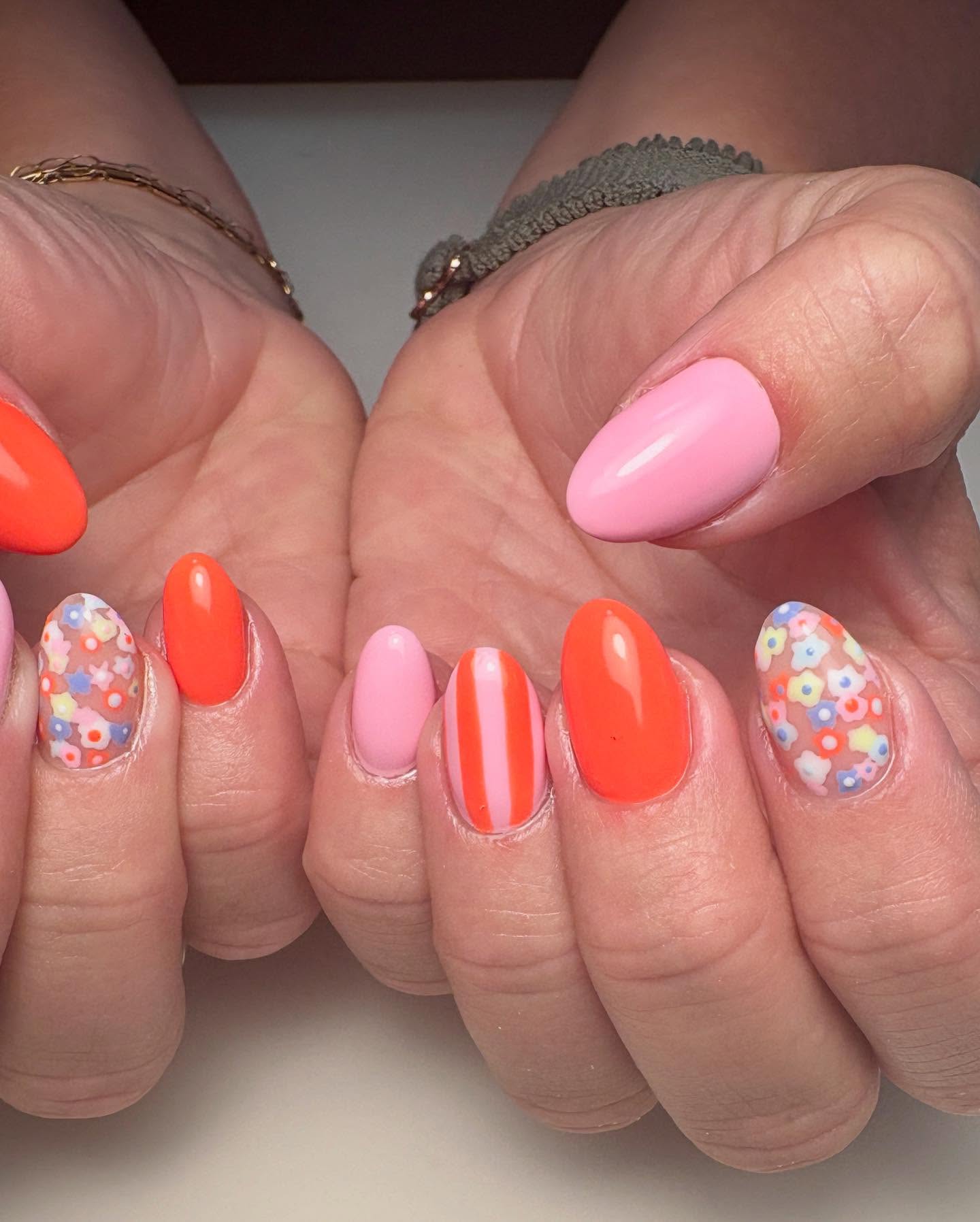 Orange and pink nails with stripe details and floral nail accents.