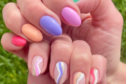 Two hands, one with solid painted nails in multiple spring colors, and the other hand with corresponding striped swirl designs.