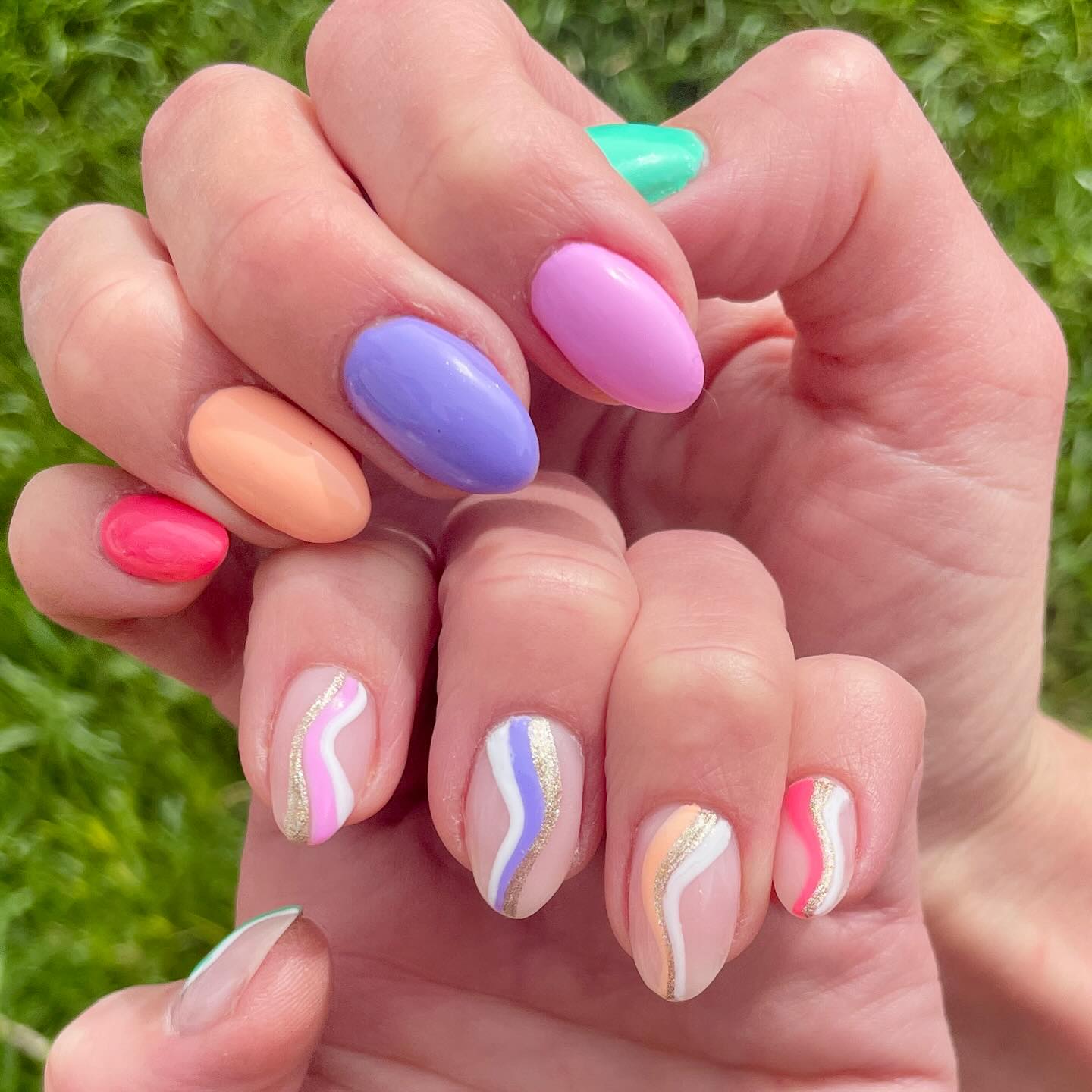 Two hands, one with solid painted nails in multiple spring colors, and the other hand with corresponding striped swirl designs.