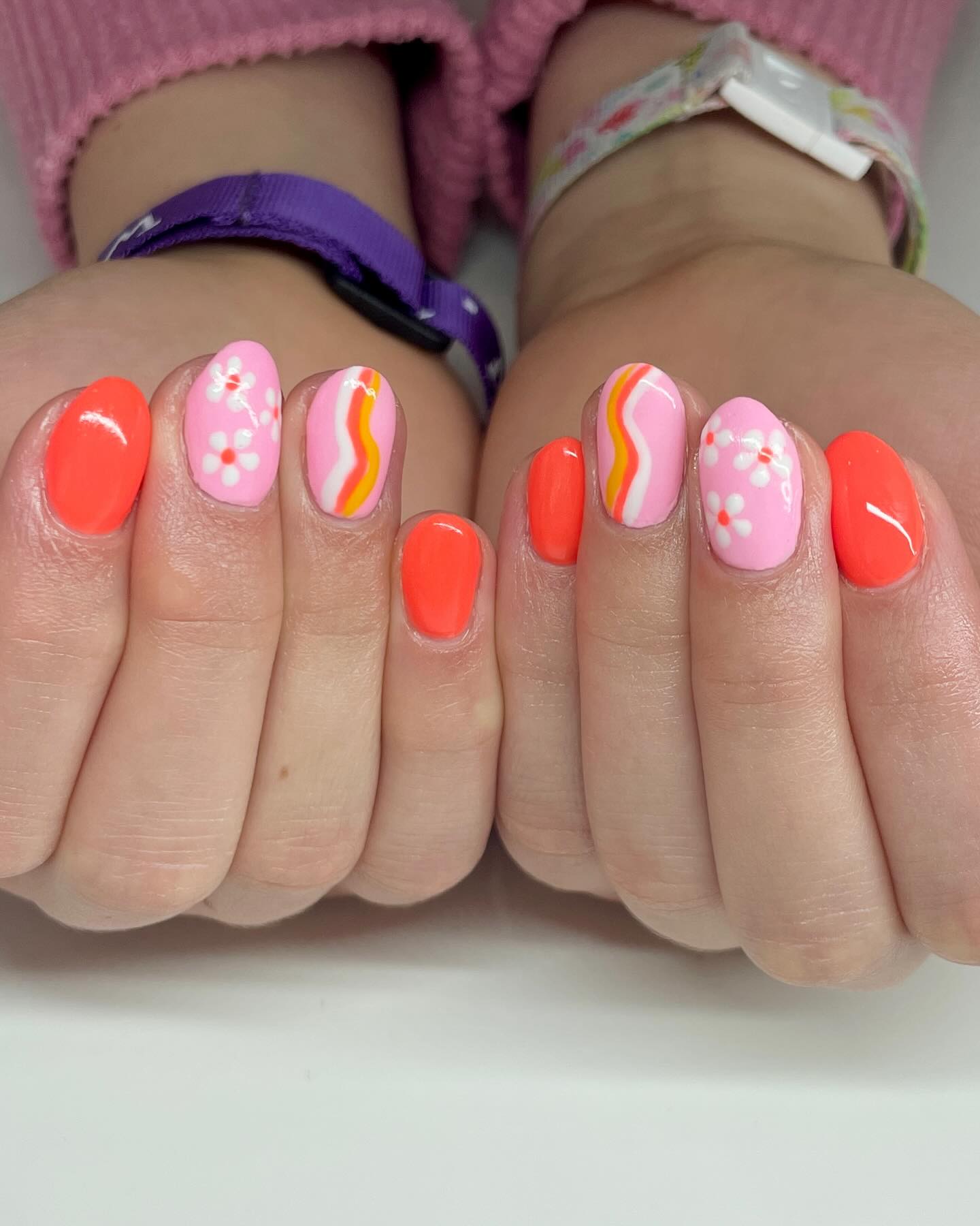 Pink and orange nails with white flowers and curvy stripe details.
