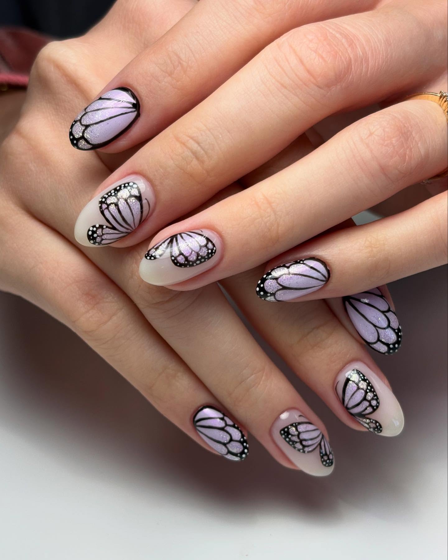 Nude almond nails with purple butterfly wings on them.