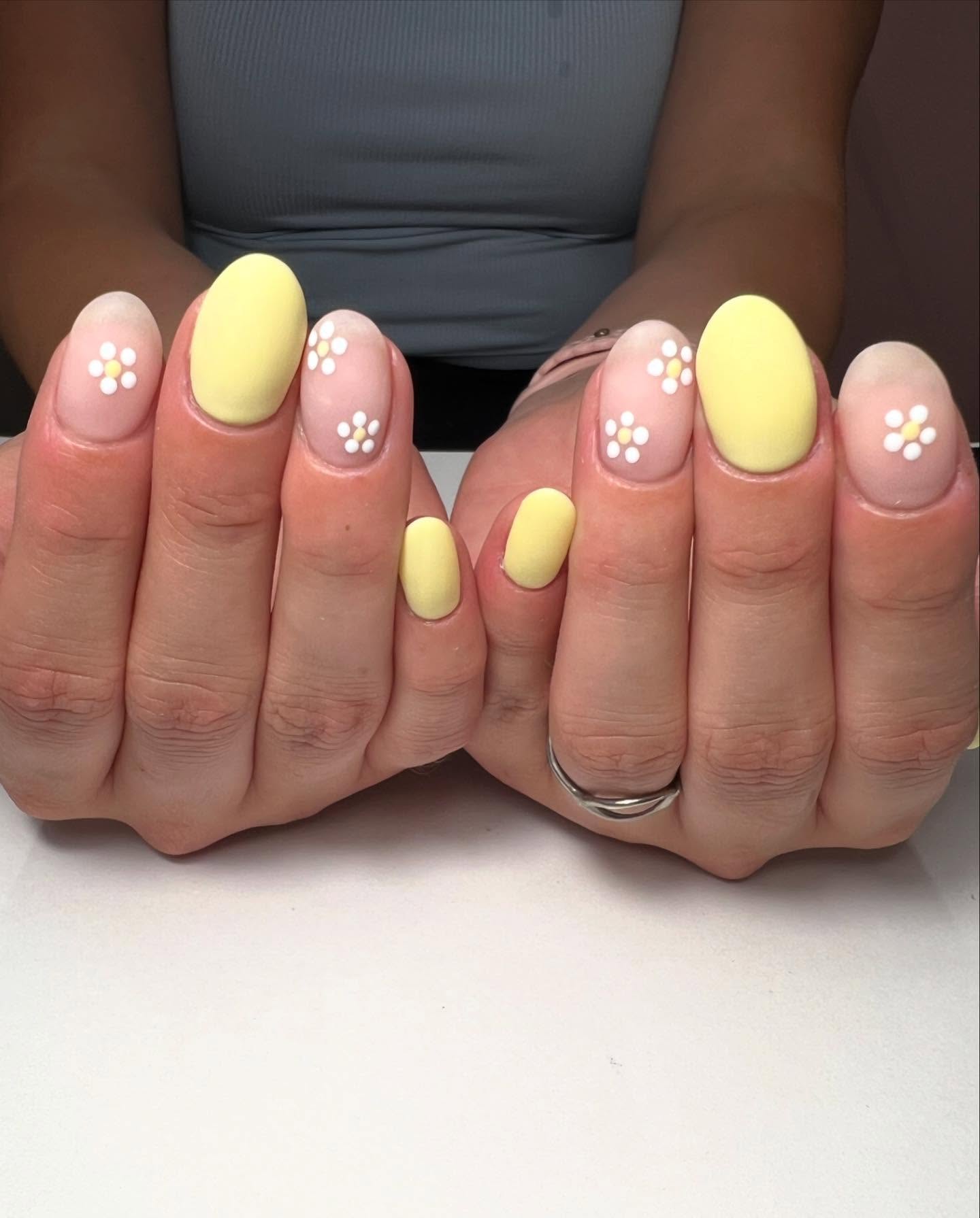 Light yellow nails with nude accent nails that have a daisy on them.