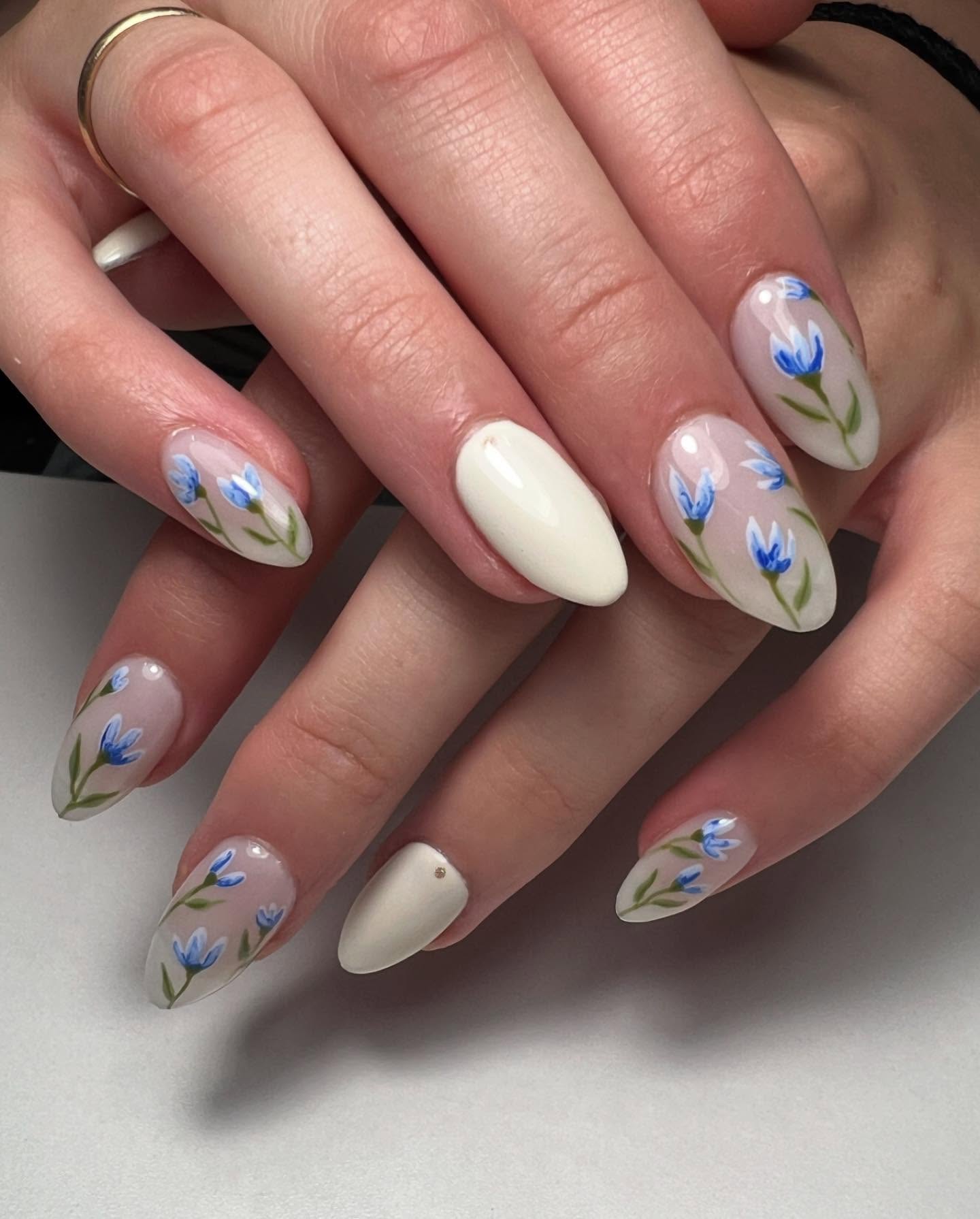 Nude nails with blue florals and a white accent nail.