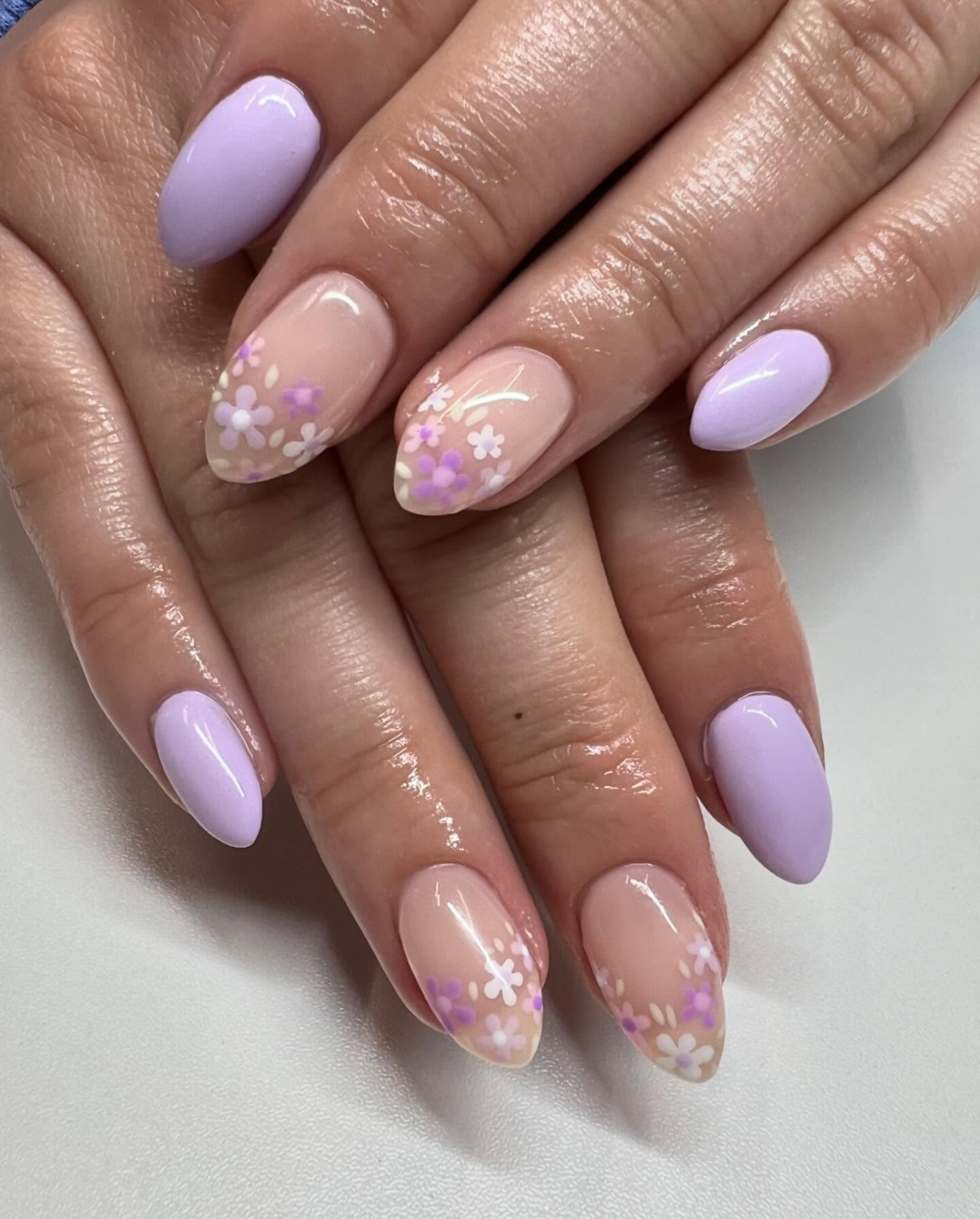 Light purple almond nails with nude accent nails that have flowers on them.