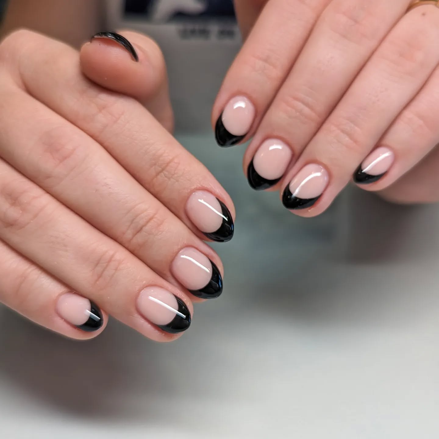 Nude almond French tip nails with black tips.
