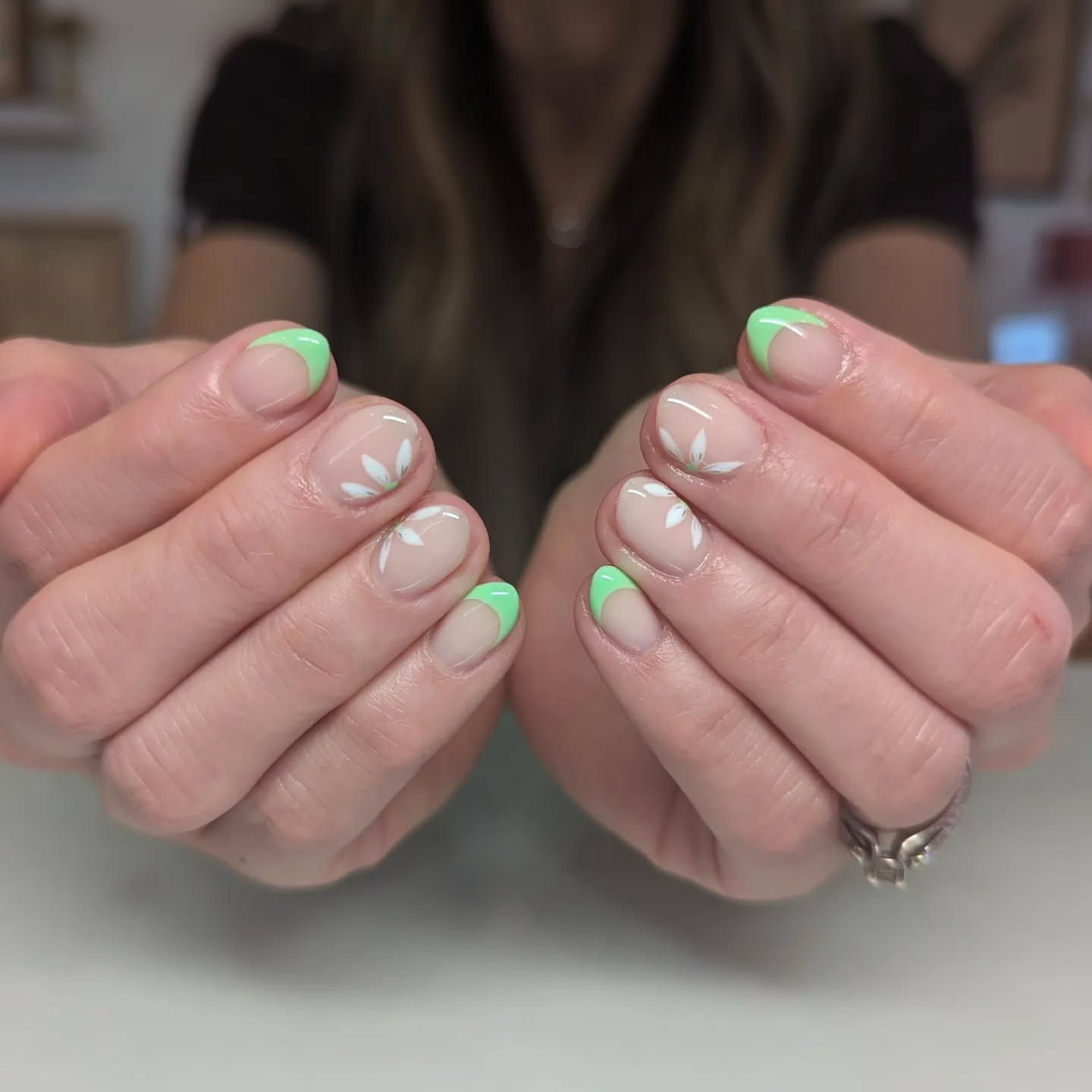 Nude almond nails with flower petals on the sides and accent nails that have a neon green French tips.
