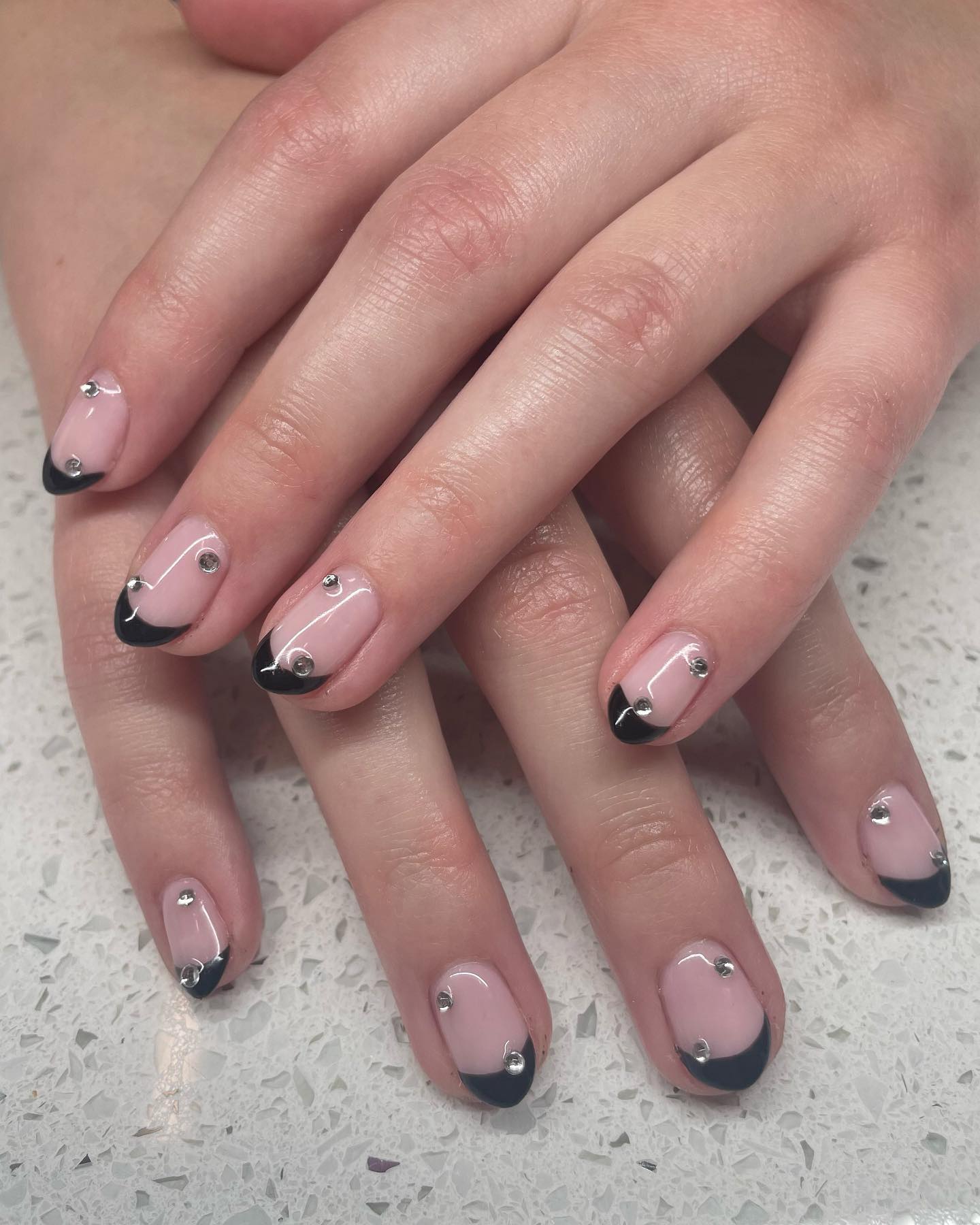 Nude almond nails with black French tips and clear rhinestones.