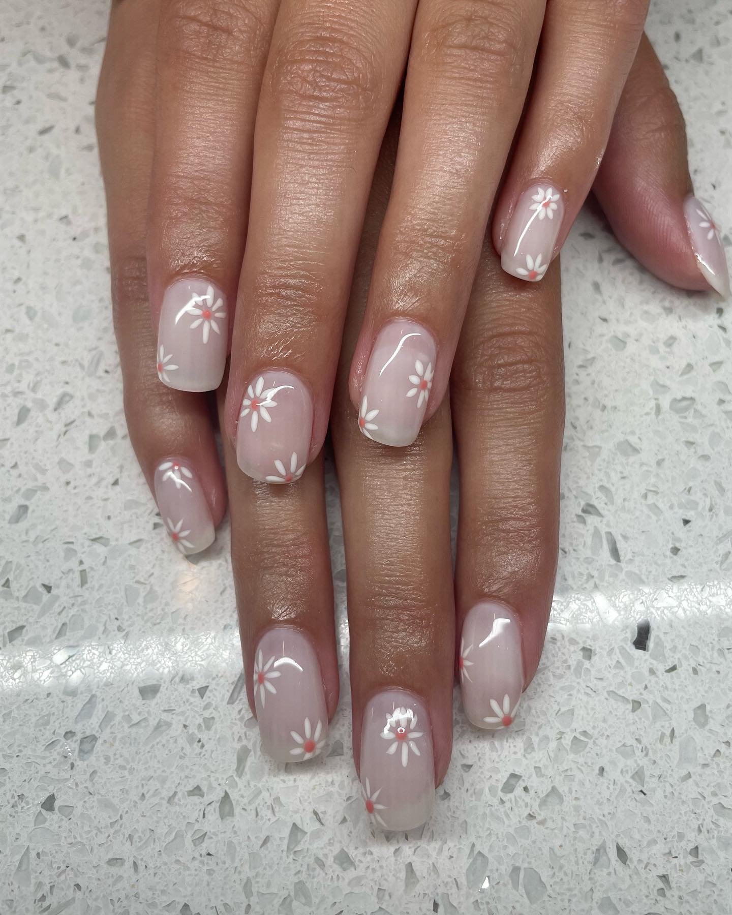Nude nails with mini daisy flower designs and pink centers.