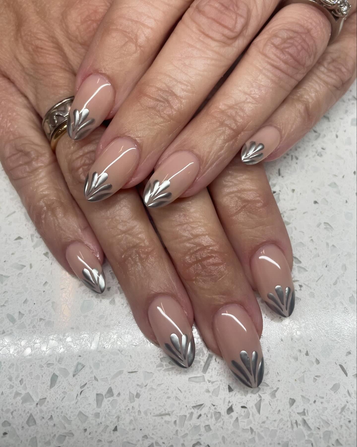 Nude almond nails with seilver petal details at the tips.