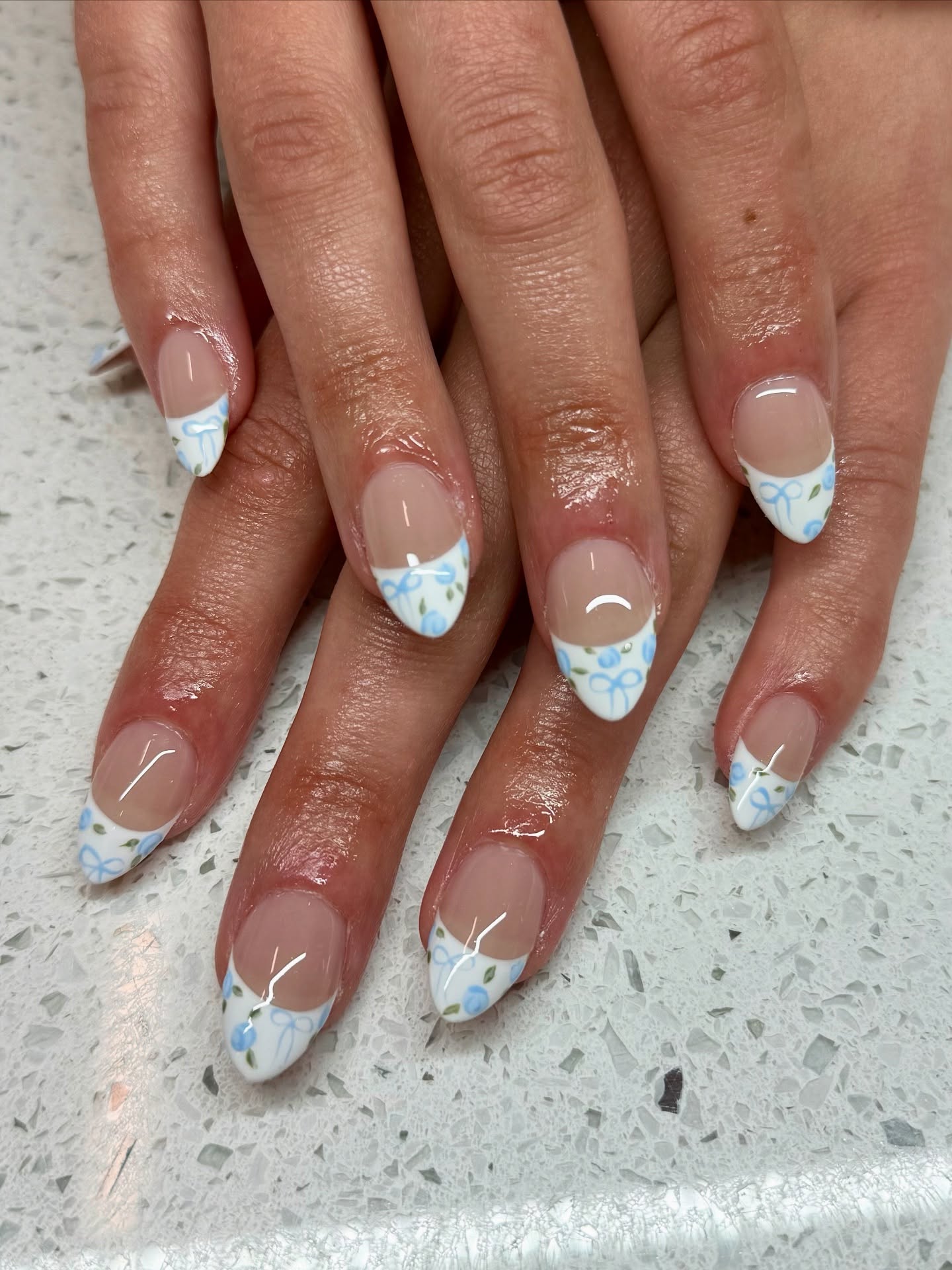 Nude nails with white French tips that have blue bow and flower details.