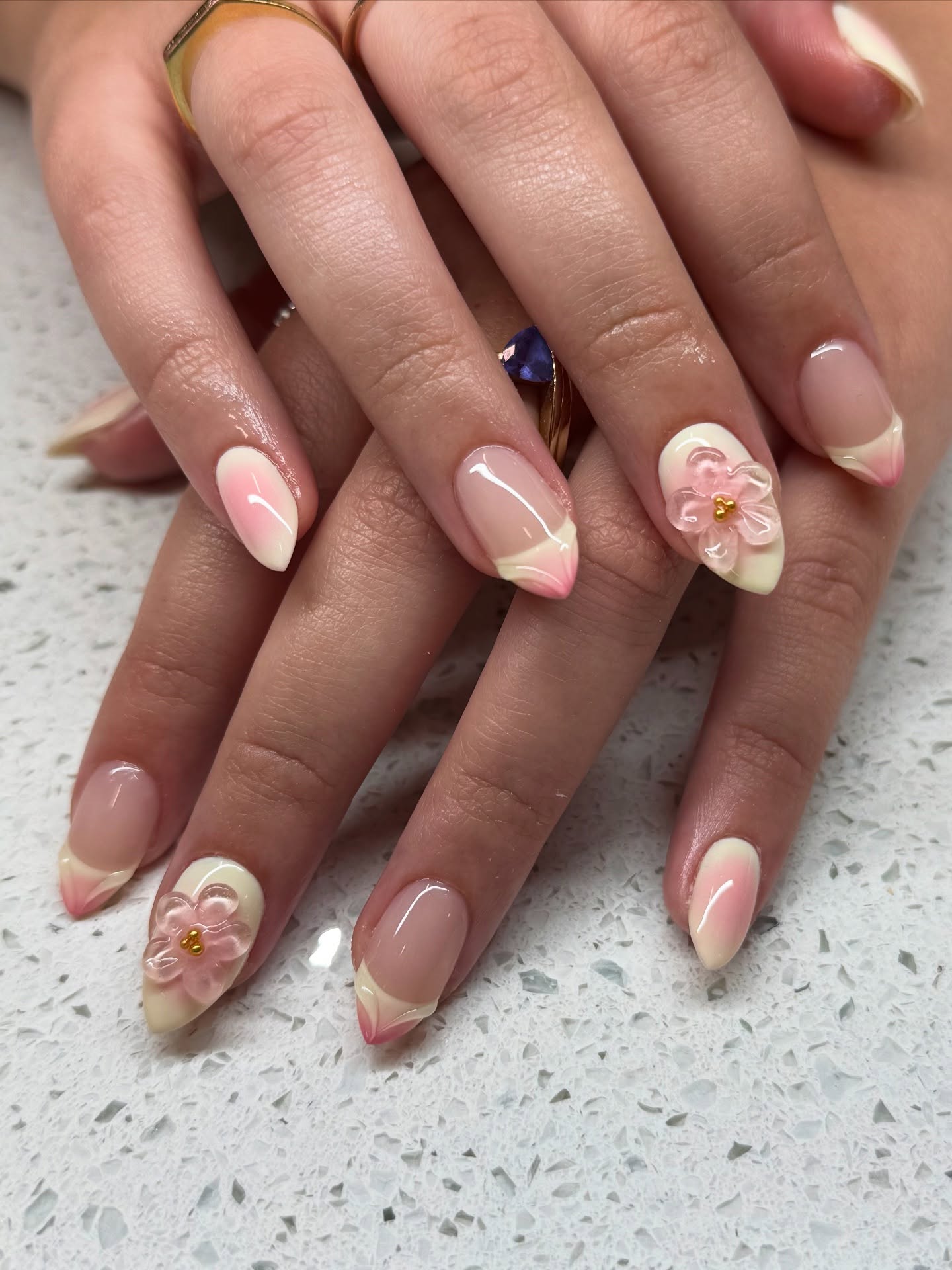 Nude nails with with yelow and pink pastel French tips and yellow accent nails that have 3D pink flowers.