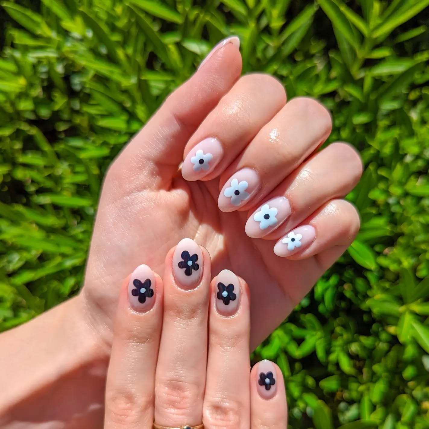 Nude nails with black daisies in the center on one hand and white on the other.