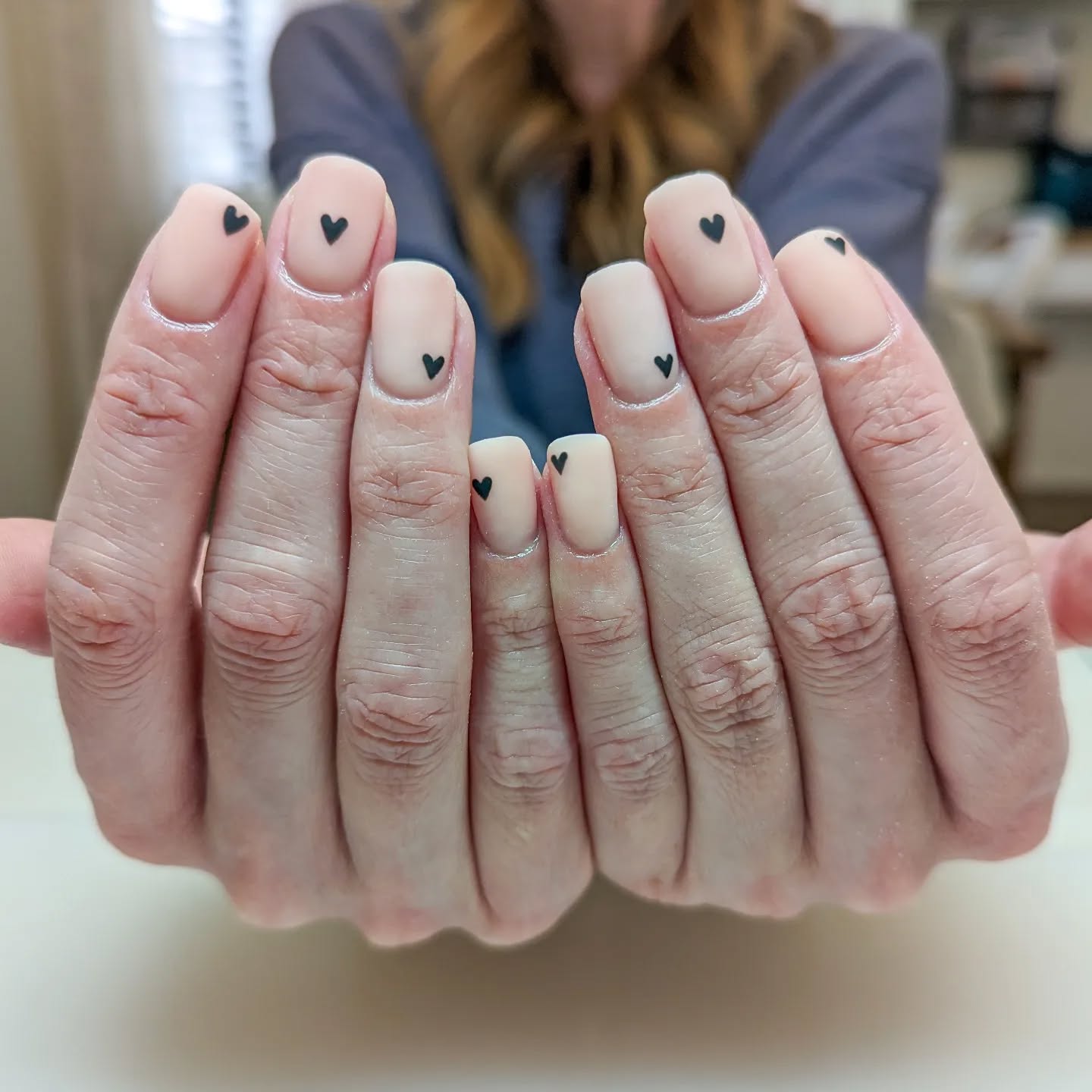 Nude square nails with one randomly placed mini black heart on each nail.