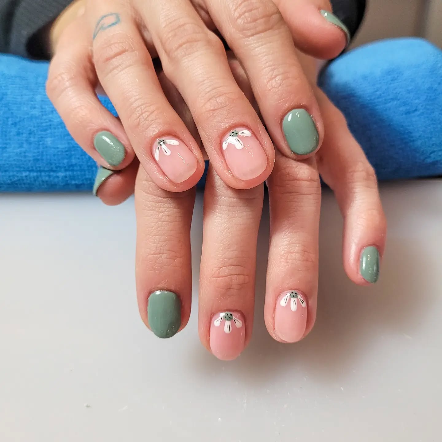 Nude nails with floral designs at the cuticles with green accent nails.