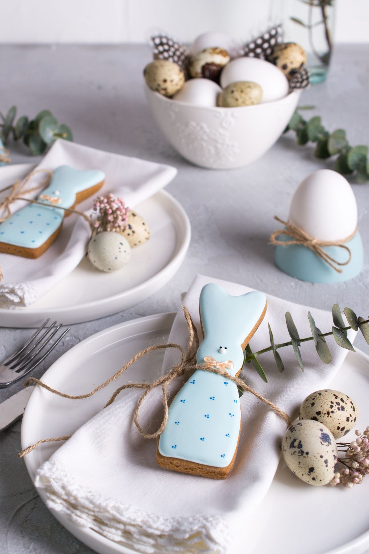 White plates with Easter bunny cookies, eucalyptus leaves, and speckled eggs.