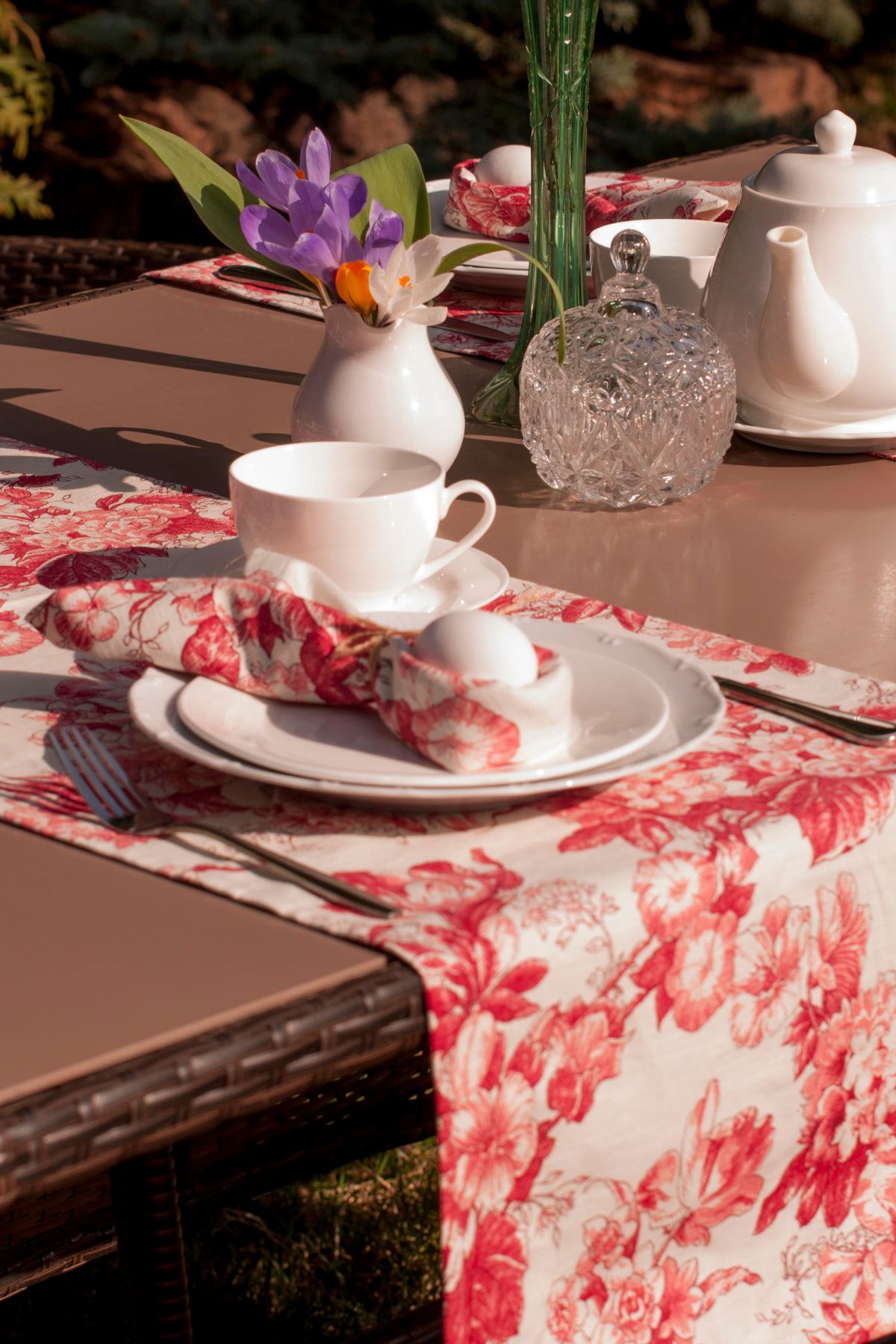 An outdoor table with a coral floral table runner and matching napkins wrapped around white eggs.