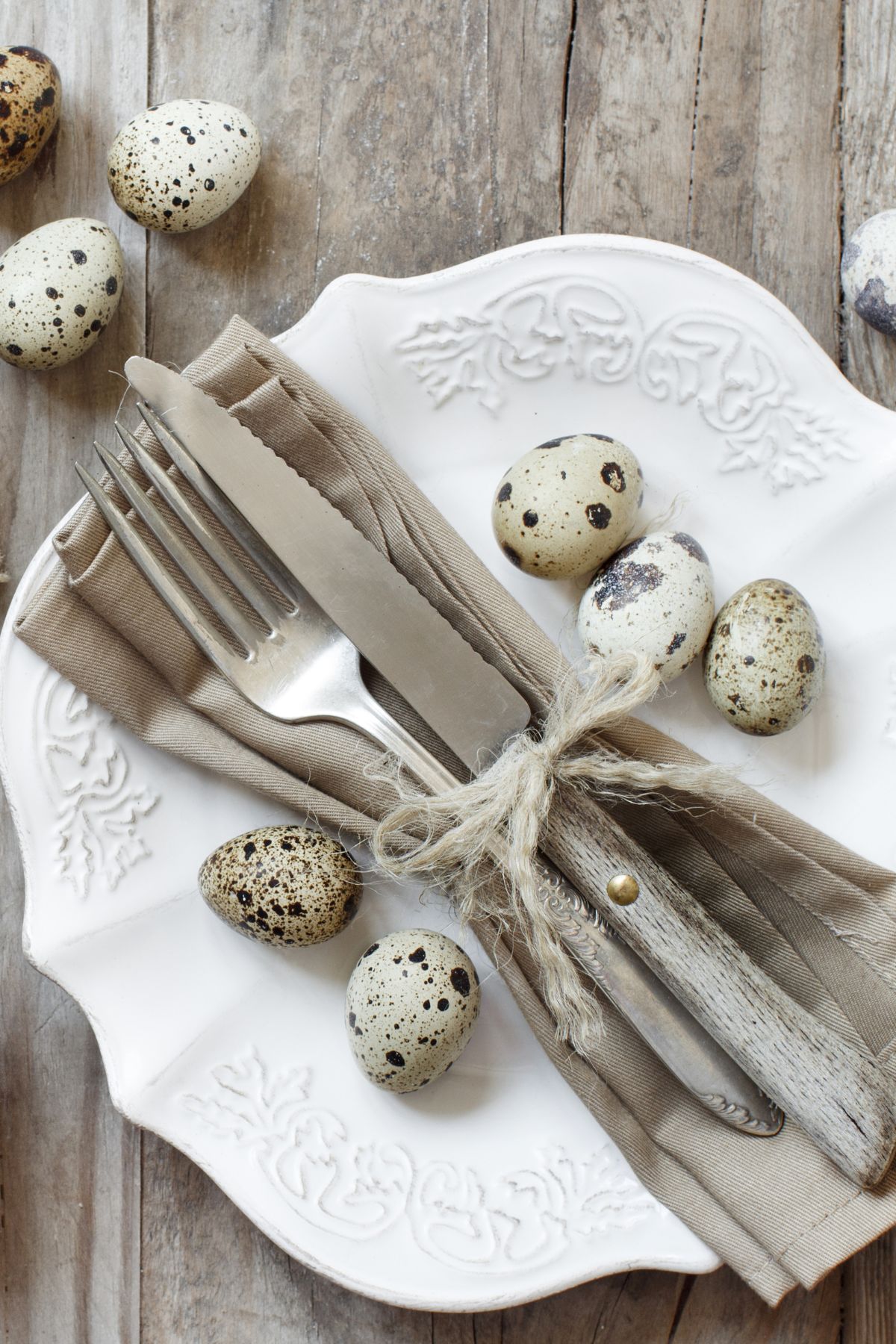 Ornate white plates with gray napkins, silverware wrapped in twine, and mini speckled eggs.