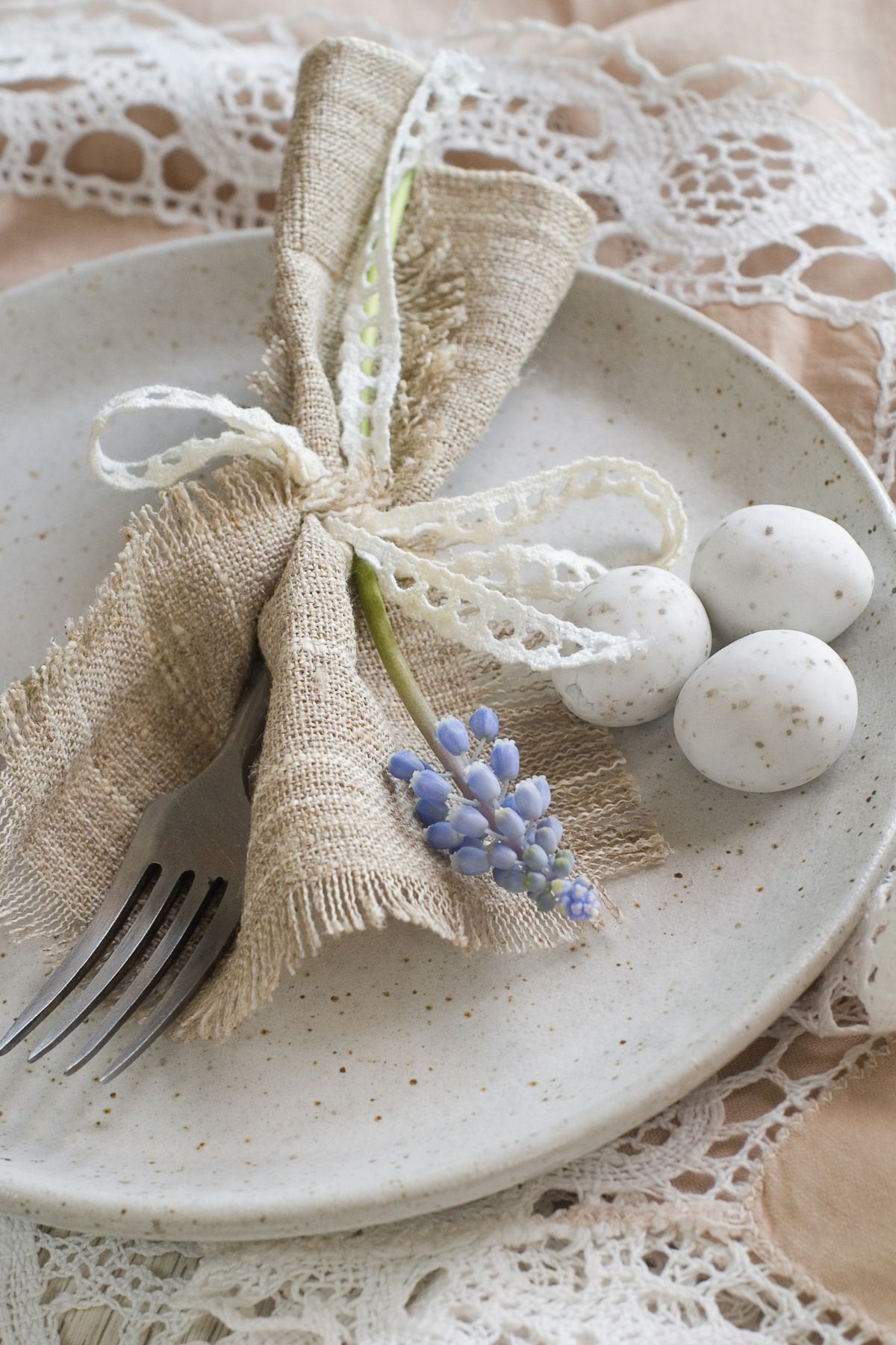A white speckled plate with a burlap napkin, lavender, and utensils wrapped in twine with mini speckled eggs.