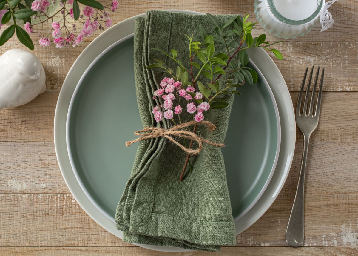 Green stacked plates with a forest green napkin wrapped in twine with spring flowers and greenery.