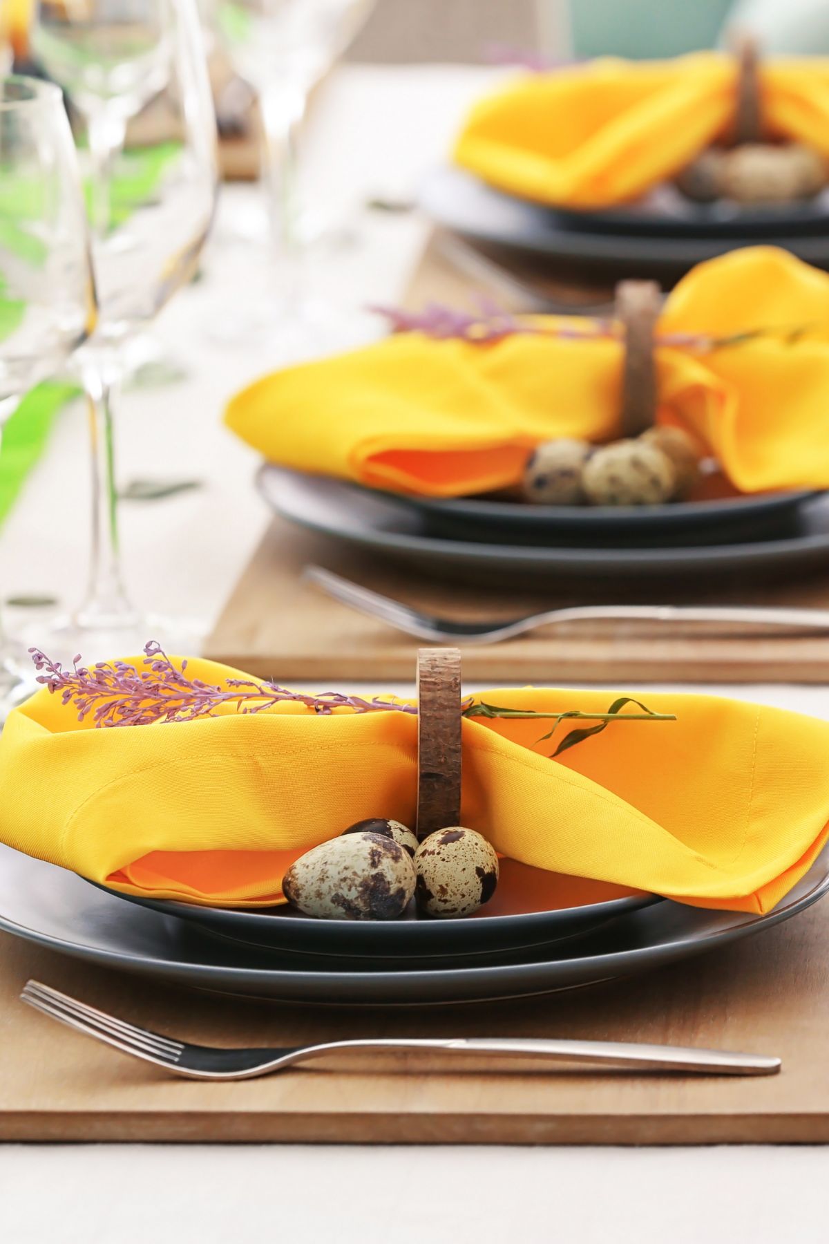 Stacked black plates with a golden yellow napkin with wood napkin rings and mini speckled eggs.