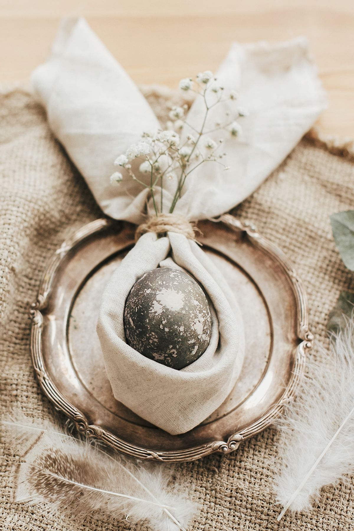 An antique silver plate with a mottled egg wrapped in a cream napkin to look like bunny ears.