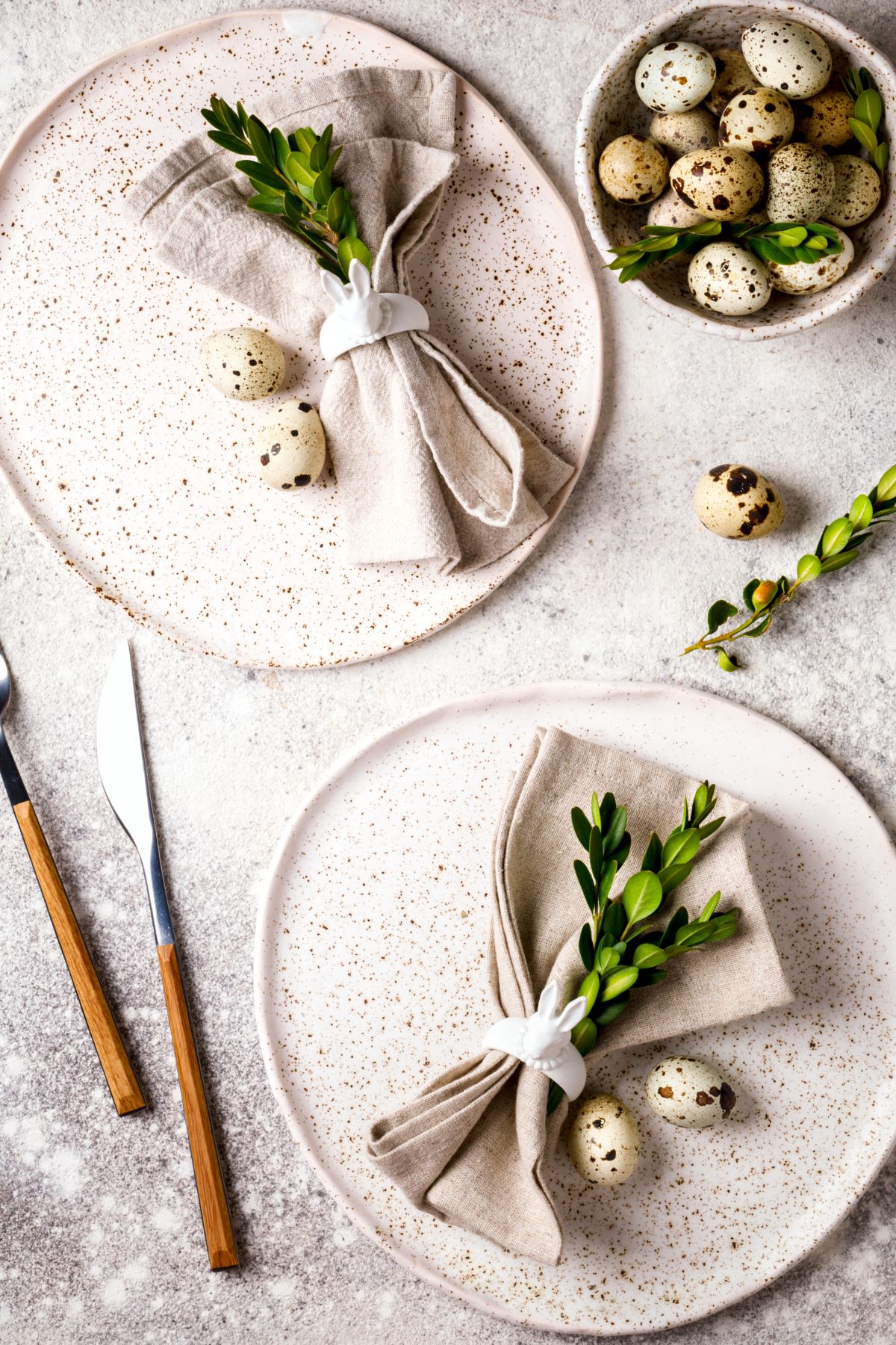 White speckled plates with cream napkins, greenery, and mini speckled eggs.