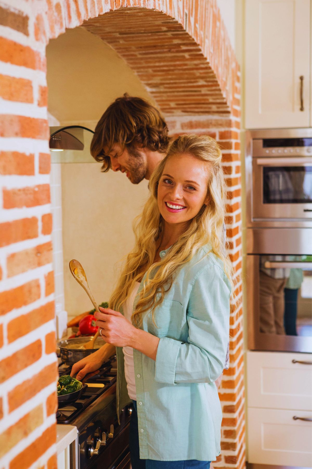 A couple cooking on a stove top that's under a brick arch.